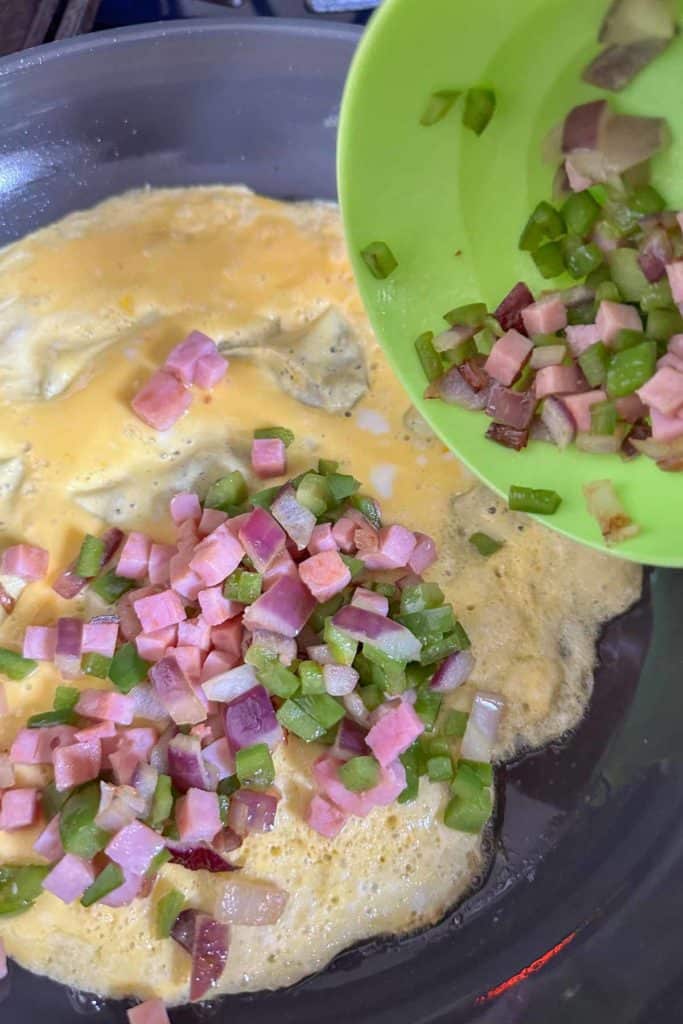 Adding ham and vegetables to an omelet cooking in a frying pan.