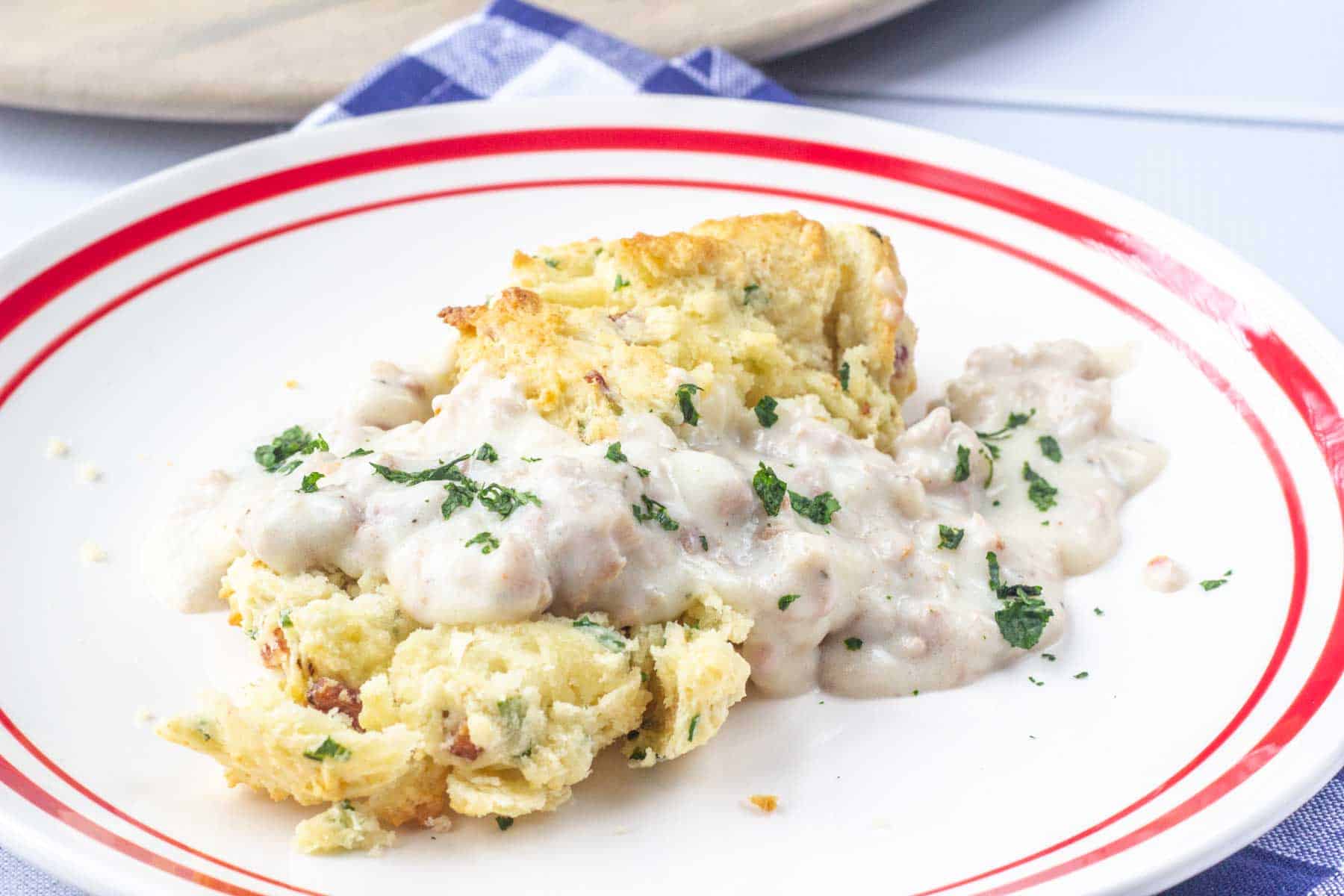 Homemade sausage gravy poured over a bacon chive biscuit on a white plate.