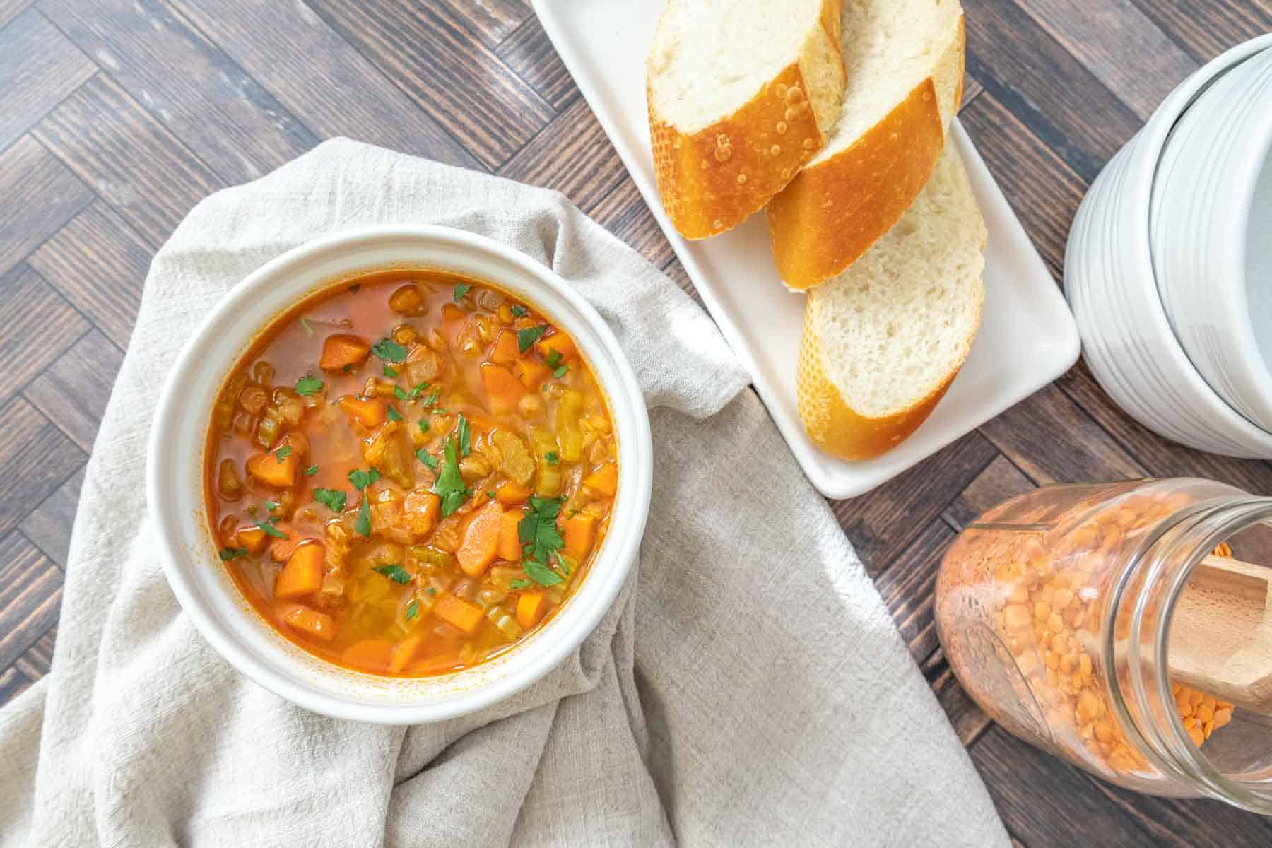 Overhead view of bowl of red lentil soup with bread and jar of lentils nearby.