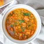 White bowl of red lentil soup with a tan napkin underneath.