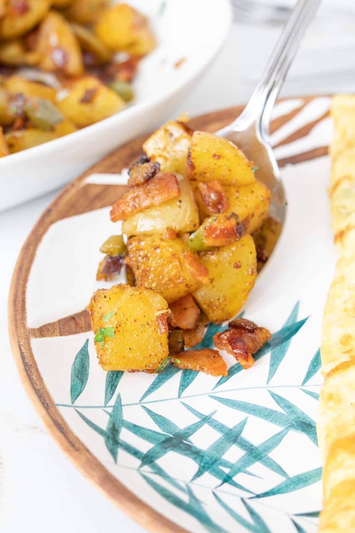 Serving spoon dishing out roasted breakfast potatoes onto a plate.