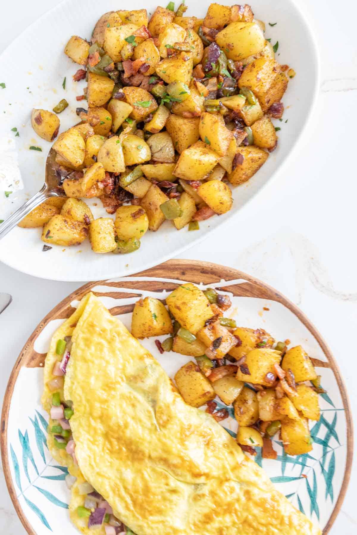 Breakfast potatoes on a serving dish next to a diner's plate with potatoes and an omelet.