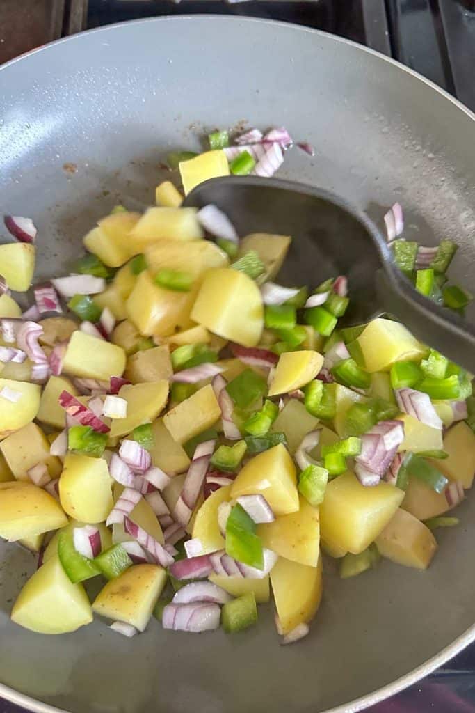 Stirring vegetables in bacon grease in a pan.