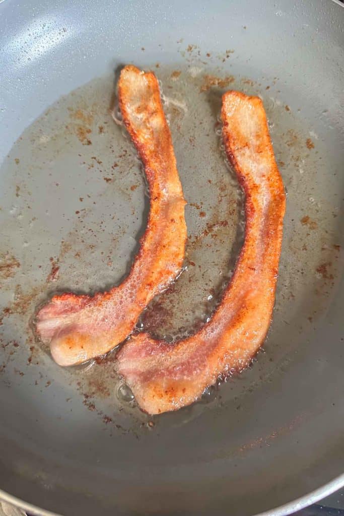 Two slices of bacon frying in a pan.
