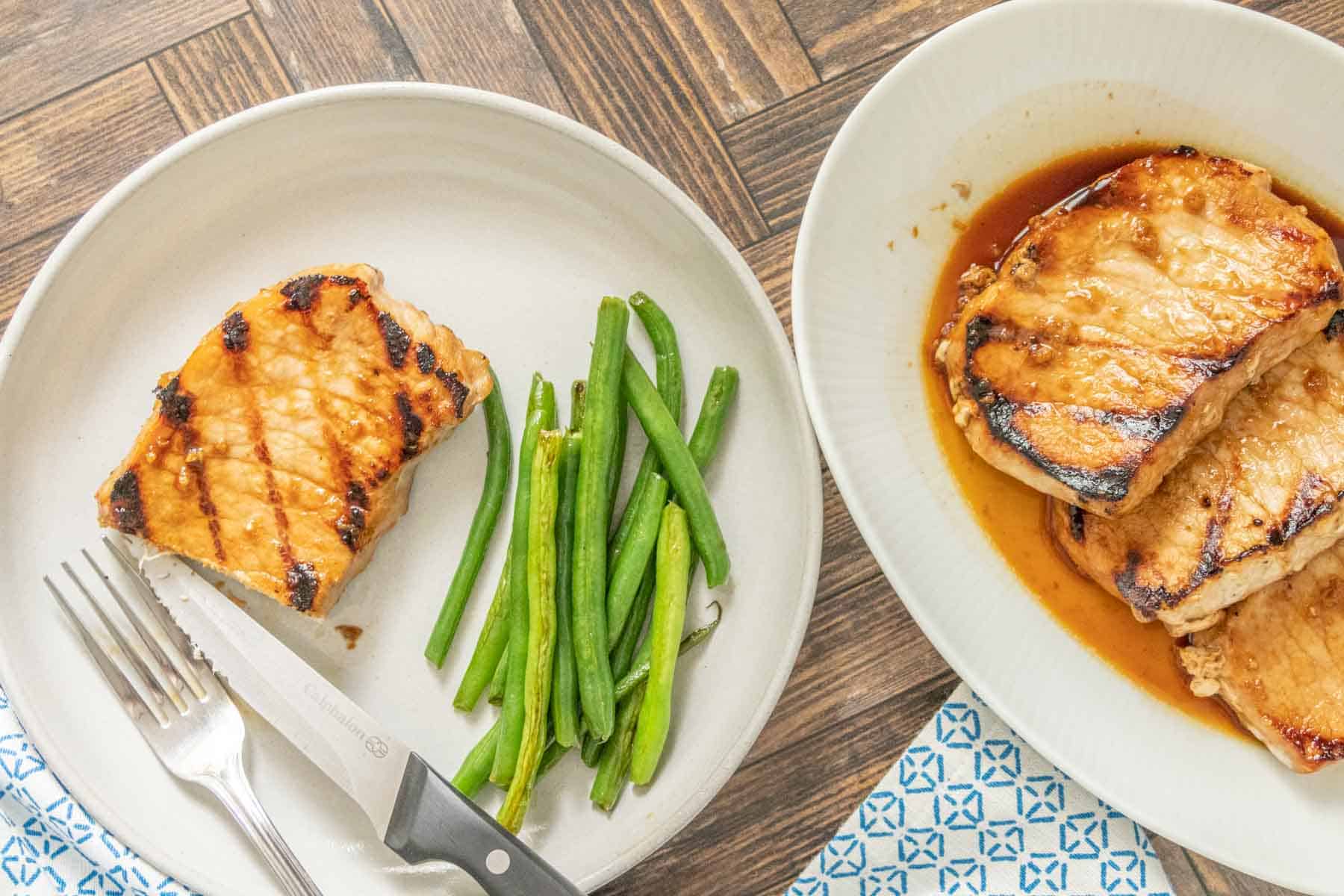 Overhead of teriyaki pork chops on a serving plate with a single serving beside partially eaten.