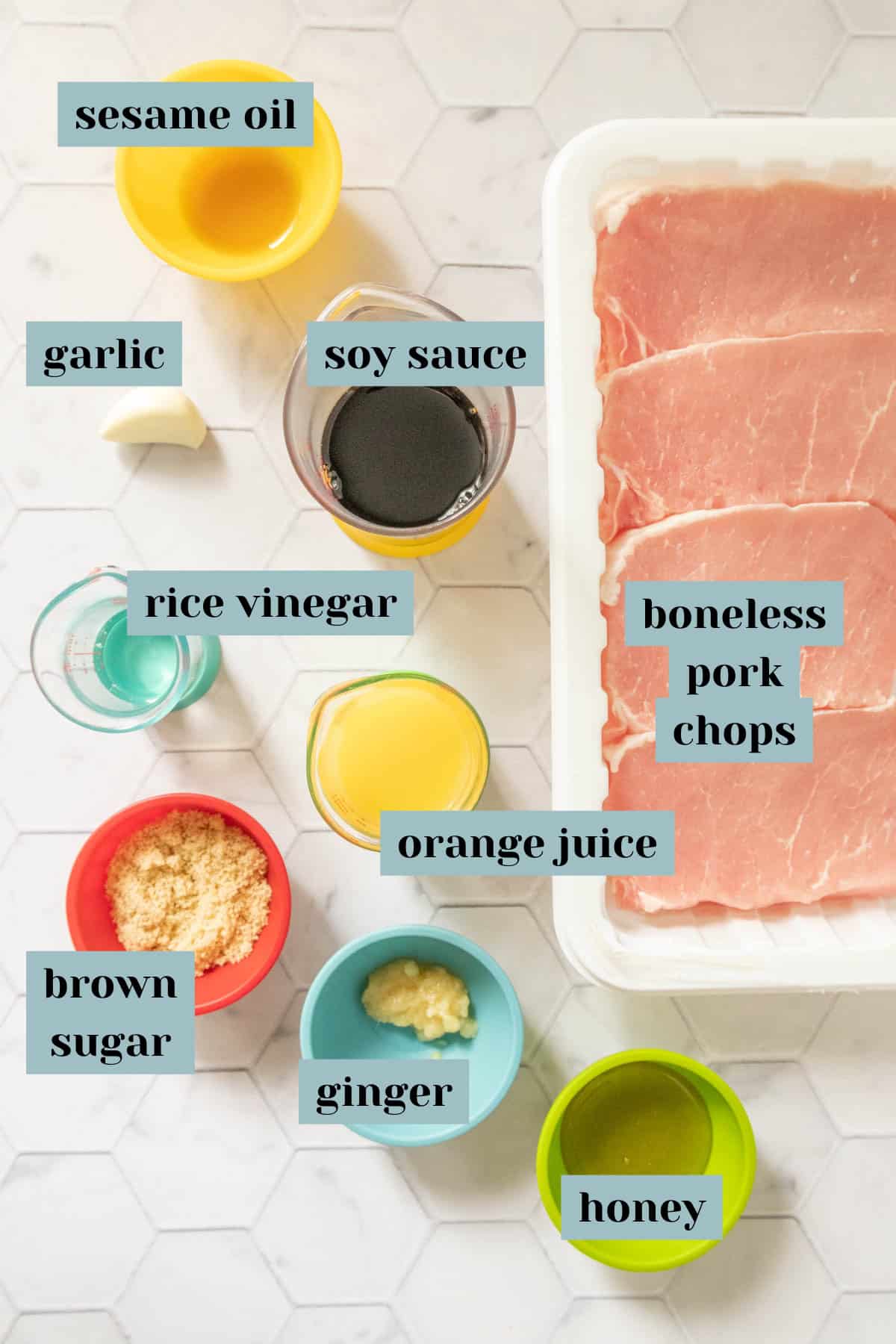 Ingredients for teriyaki pork chops on a tile surface with labels.