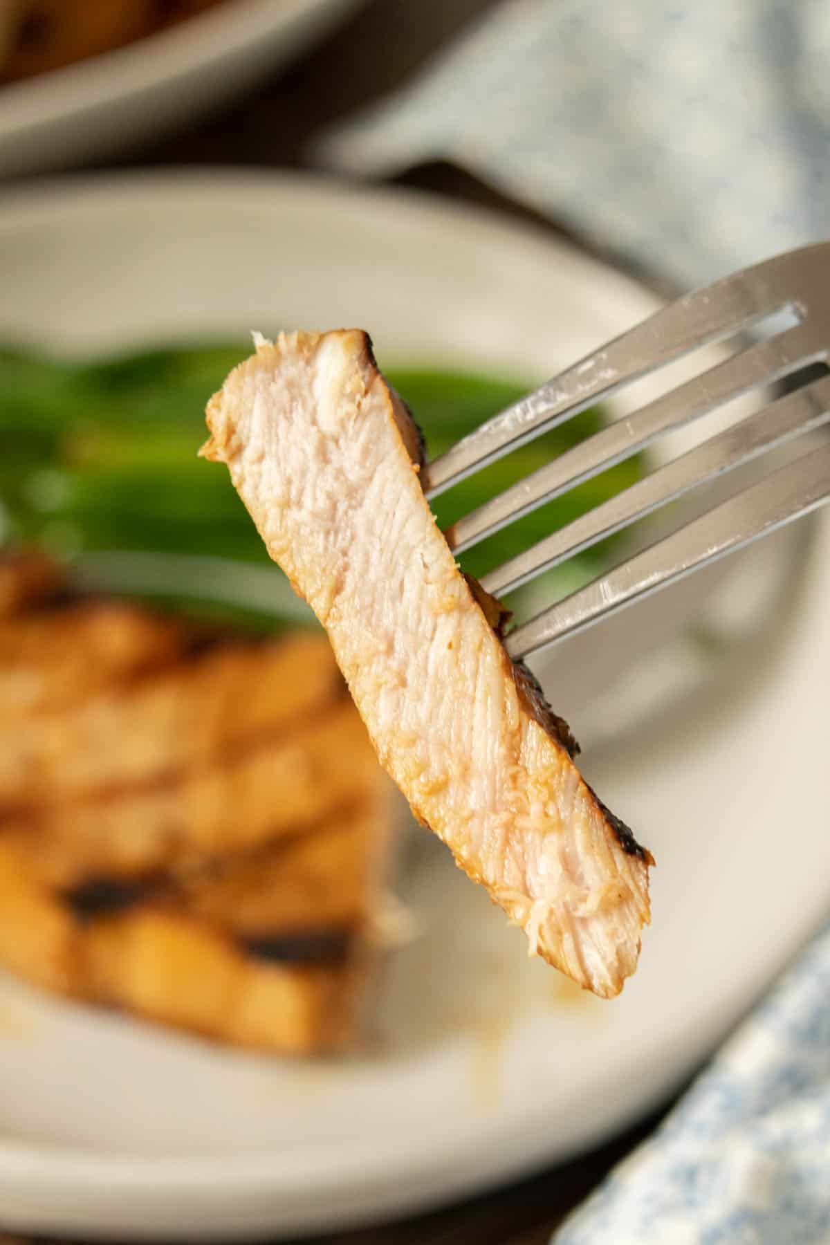 Fork holding up cut slice of teriyaki pork chop.