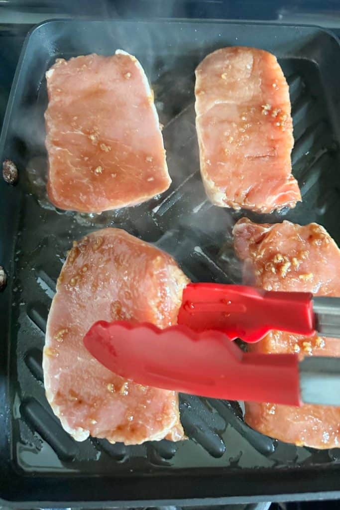 Pork chops cooking on a grill pan.