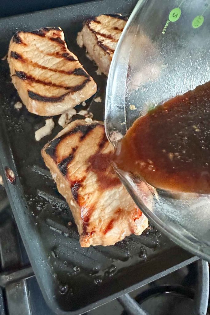 Pouring teriyaki sauce onto cooking pork chops.