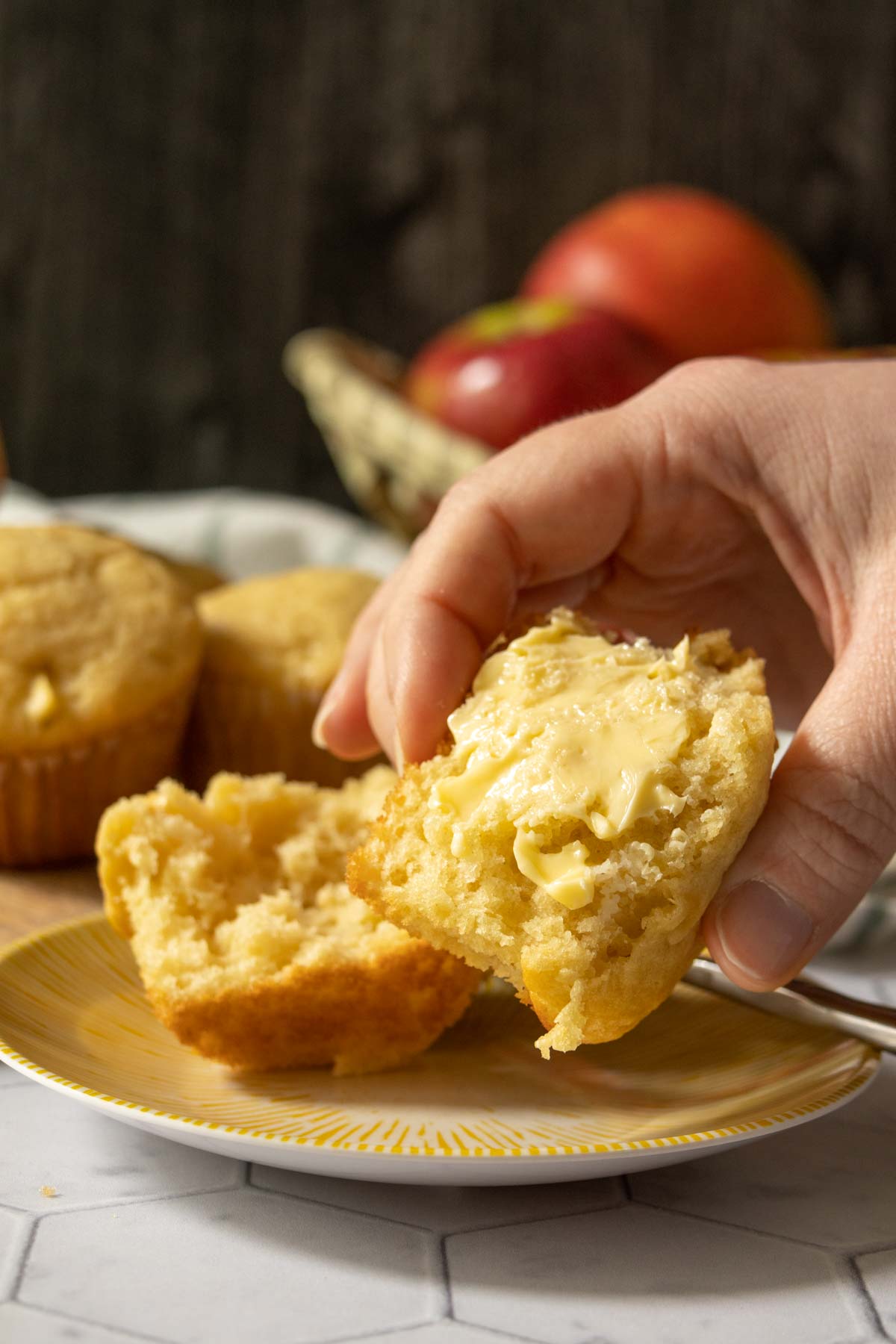 Caucasian hand holding up half an apple muffin with butter spread on it.