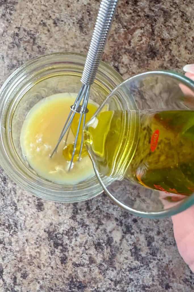 Pouring olive oil into dressing to emulsify.