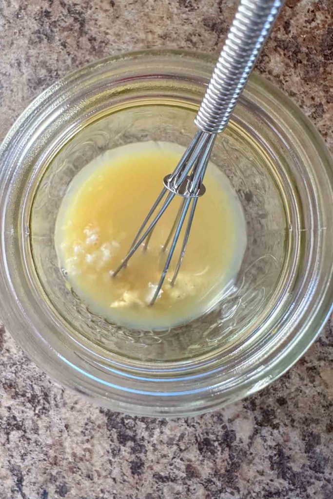 Small jar with dressing ingredients and whisk.