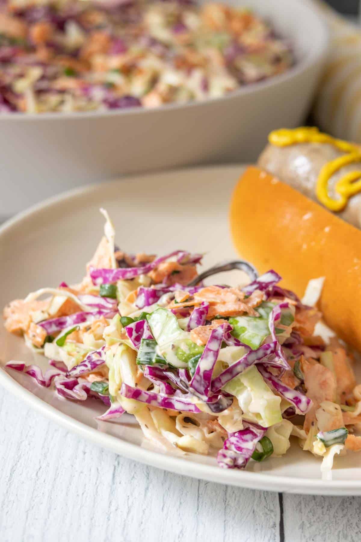 Plate with a serving of homemade coleslaw alongside a sausage in a bun.