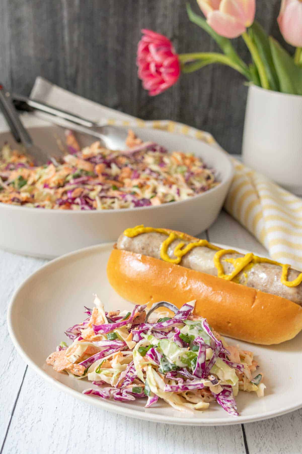 Cream plate with homemade coleslaw and a sausage in a bun.