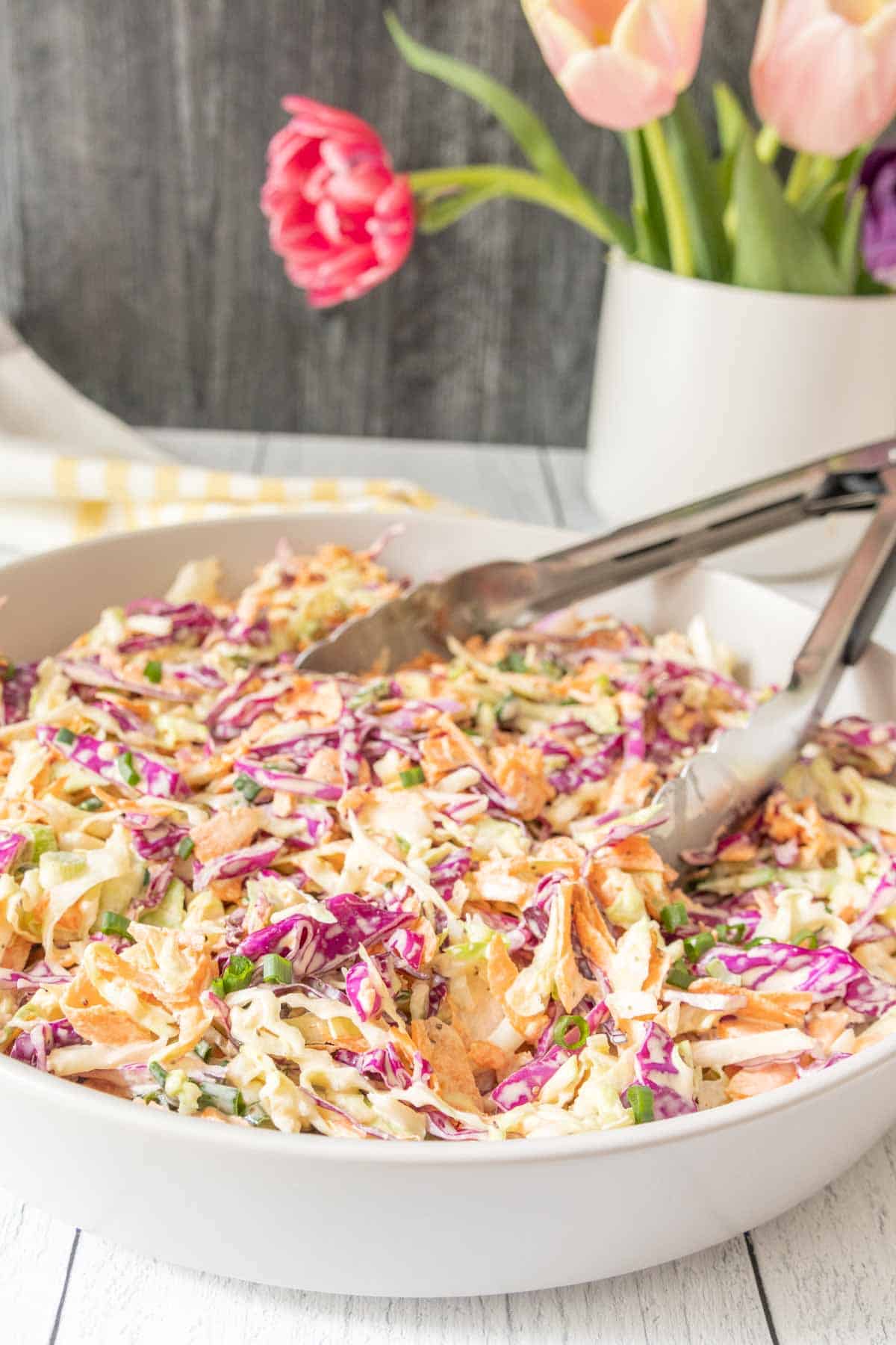 Shallow serving bowl filled with homemade coleslaw with tongs.