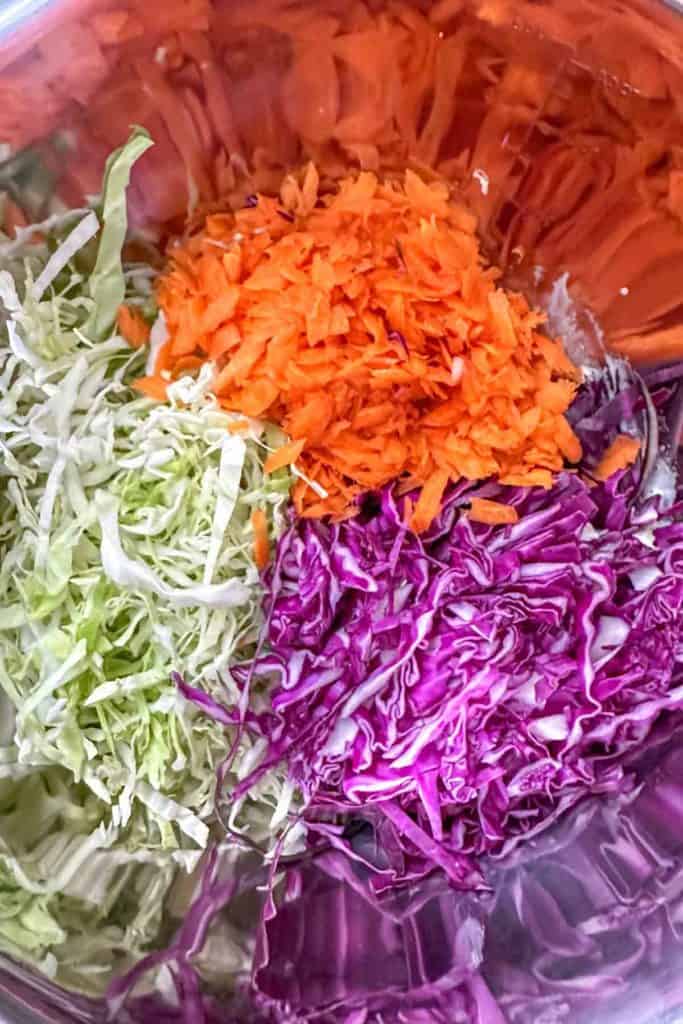 Shredded purple and green cabbage with grated carrot in a metal mixing bowl.