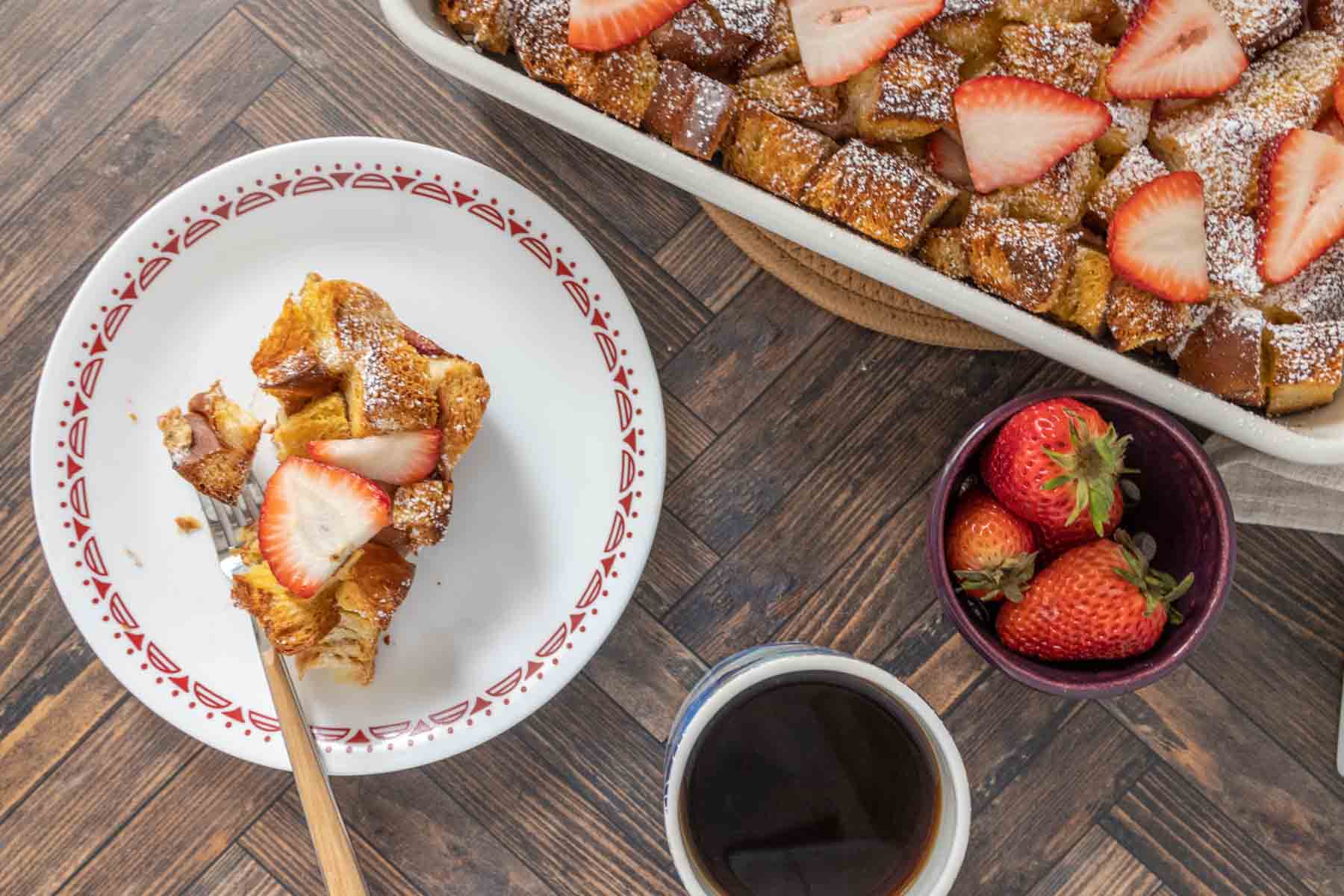 Overhead of strawberry french toast on a plate with coffee and the full dish beside.