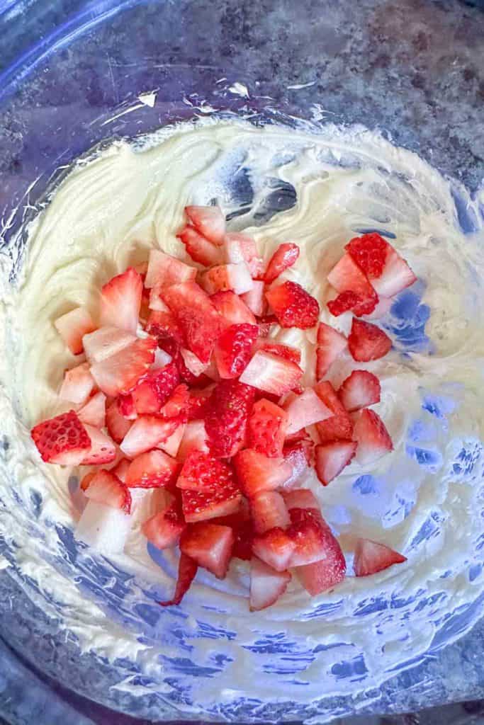 Chopped strawberries and whipped cream cheese in a blue mixing bowl.