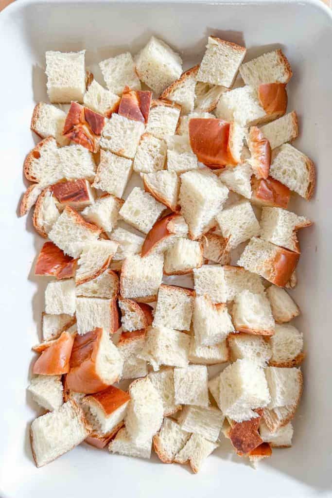 Layer of bread cubes in a white casserole dish.