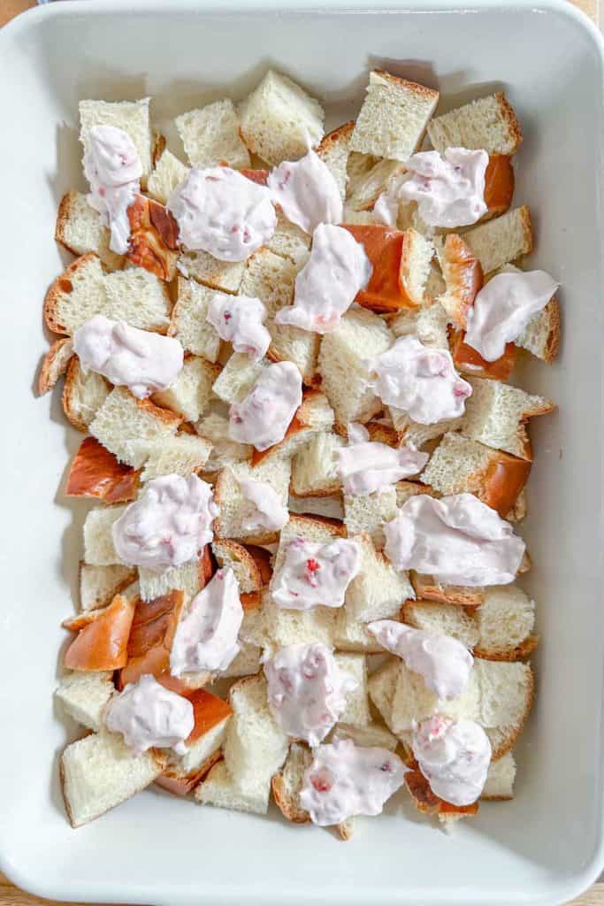 Bread cubes and dollops of strawberry cream cheese in a casserole dish.