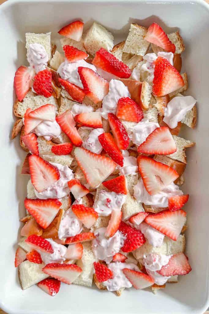 Bread cubes, cream cheese, and sliced strawberries in a casserole pan.