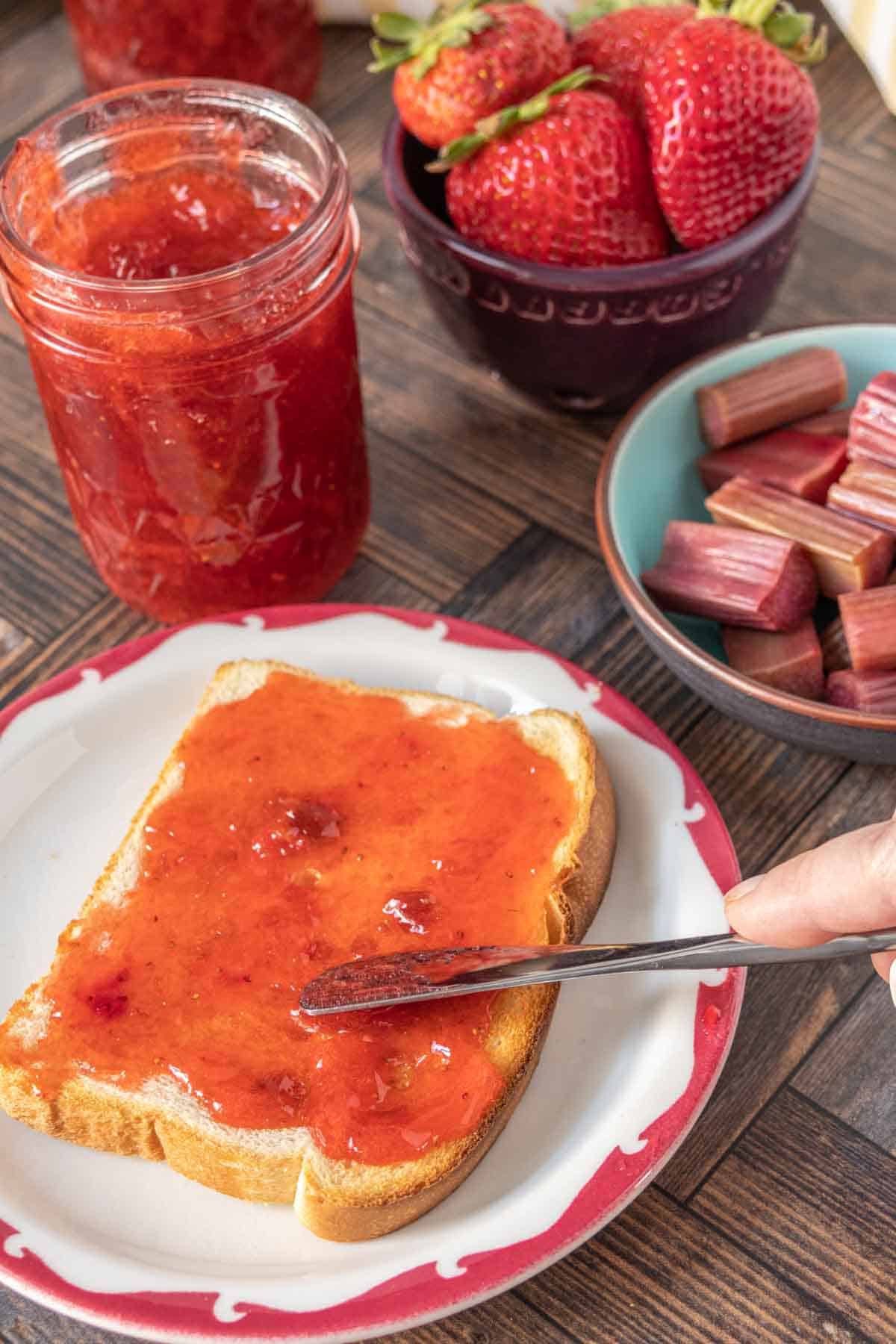 A small spreading knife being used to put jam onto a slice of white toast.