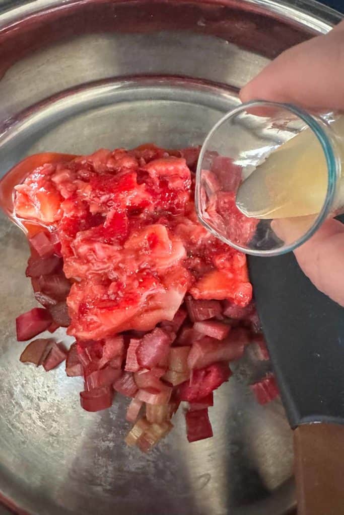 Lemon juice being poured over rhubarb and strawberries in a saucepan.