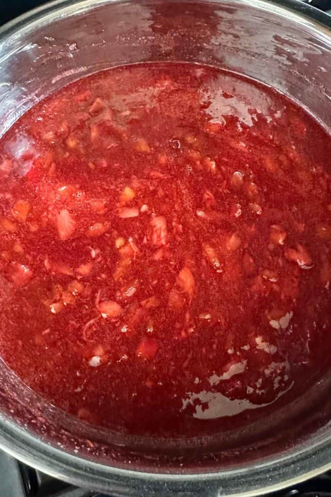 Stainless saucepan with strawberry rhubarb jam being cooked in it.