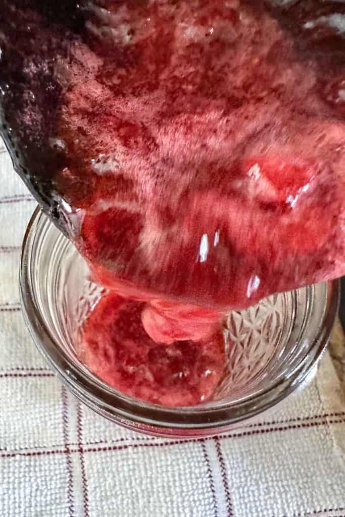 Pouring cooked jam into a glass jar from overhead.