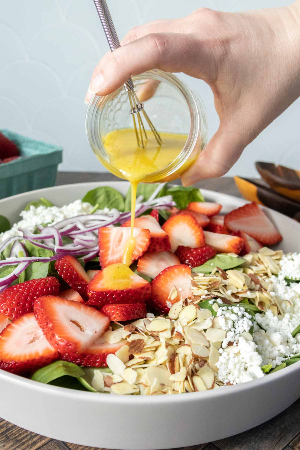 Pouring dressing onto strawberry spinach salad.