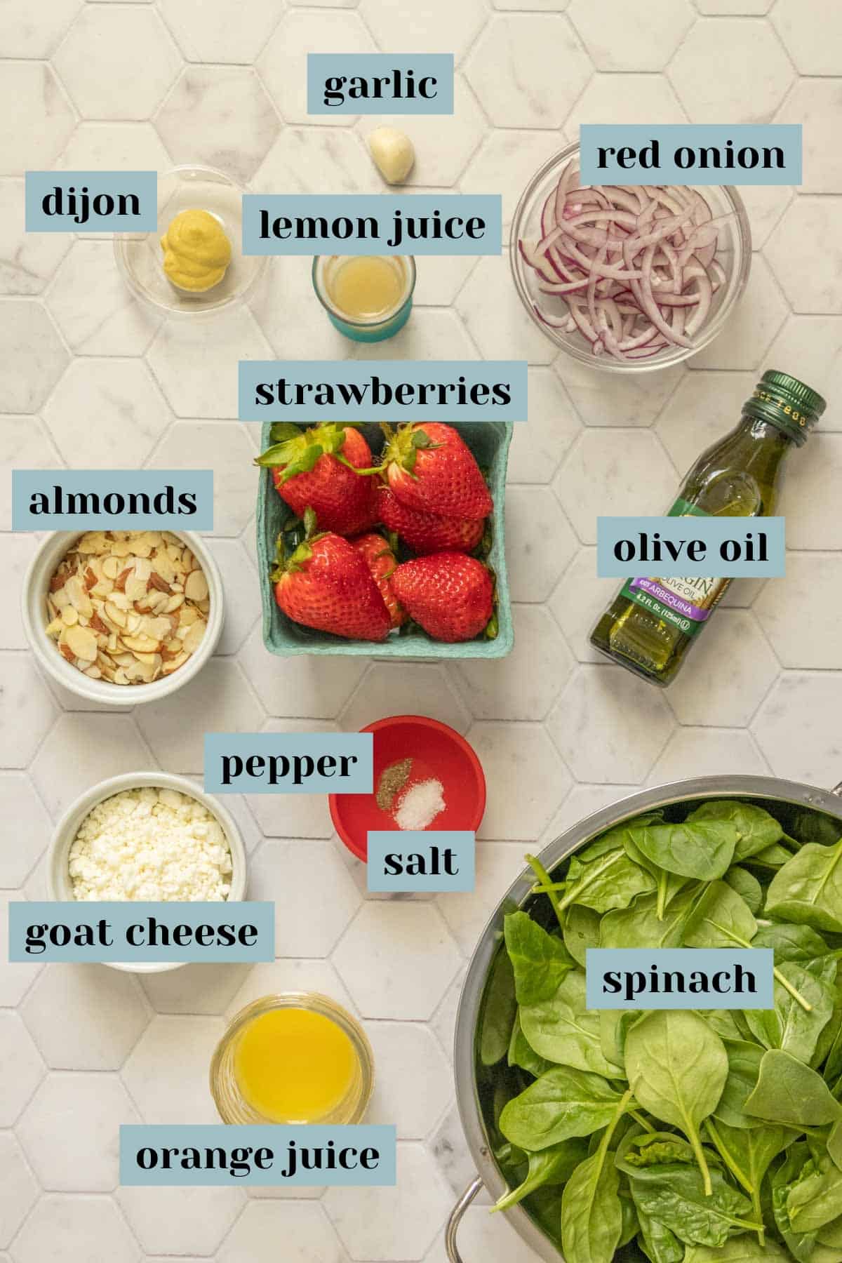 Ingredients for strawberry spinach salad on a tile surface with labels.