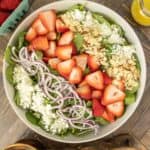 Overhead of strawberry spinach salad in a large bowl with salad servers beside.