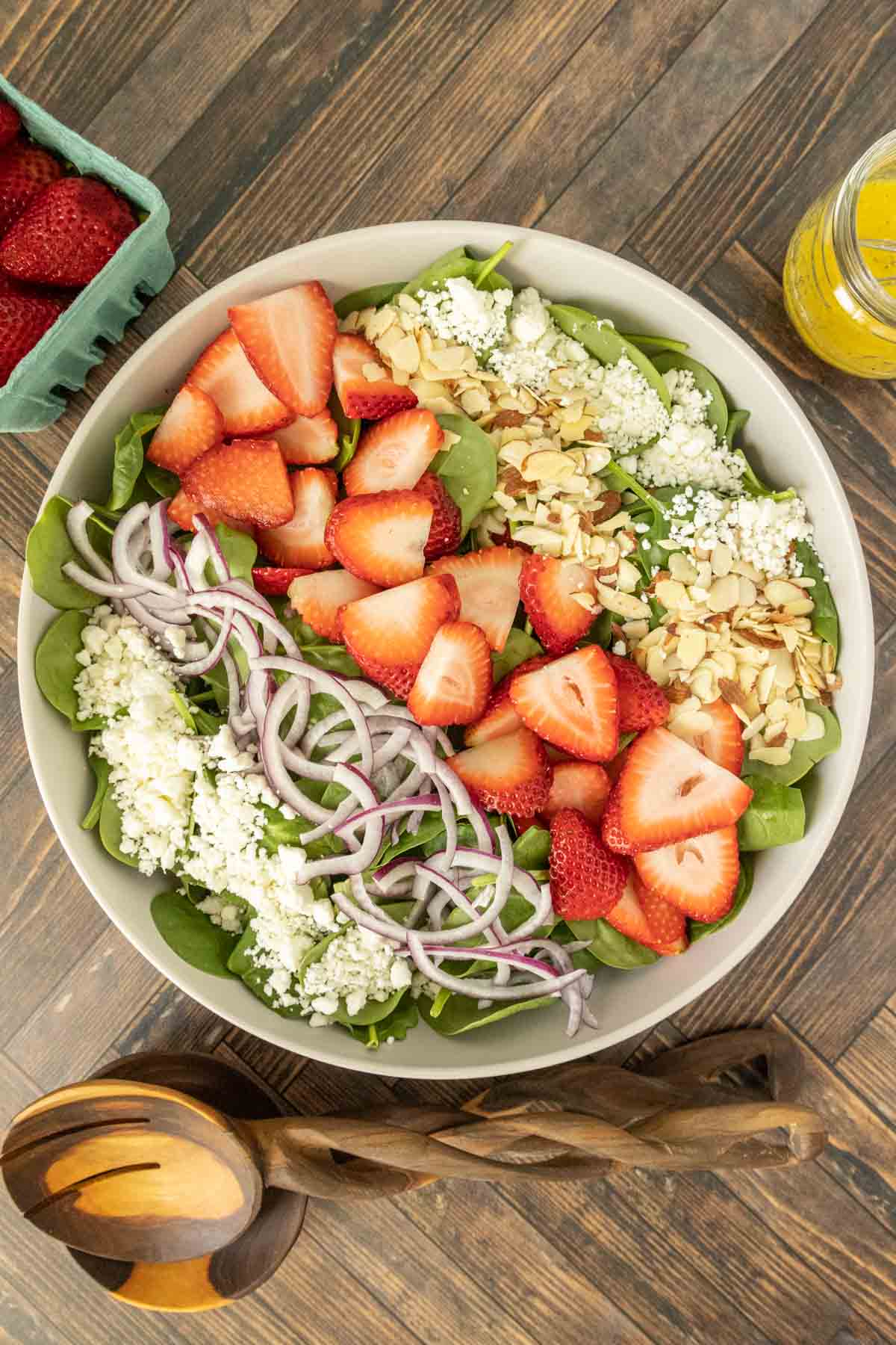 Overhead of strawberry spinach salad in a large bowl with salad servers beside.