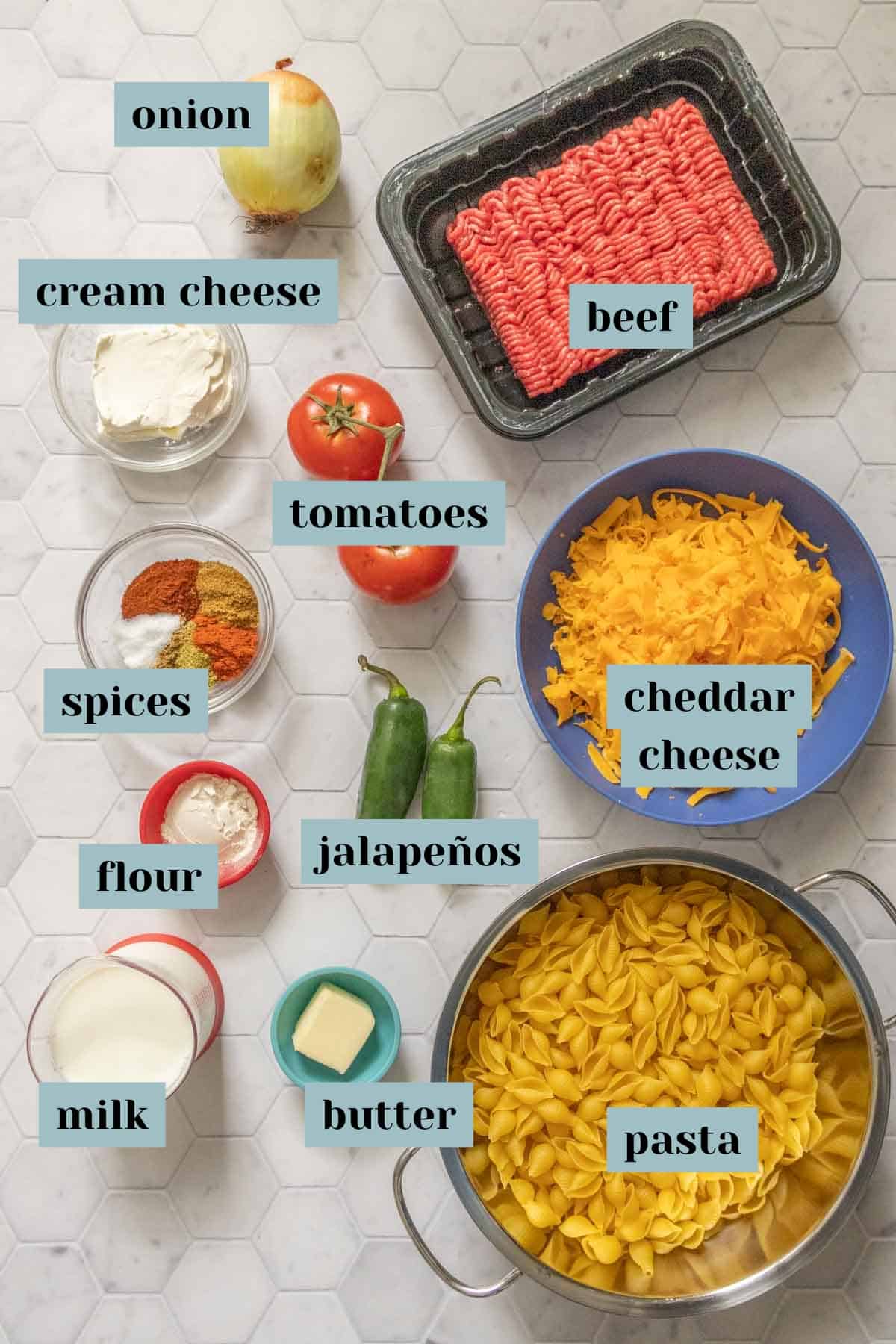 Ingredients for taco mac and cheese on a tile surface with labels.
