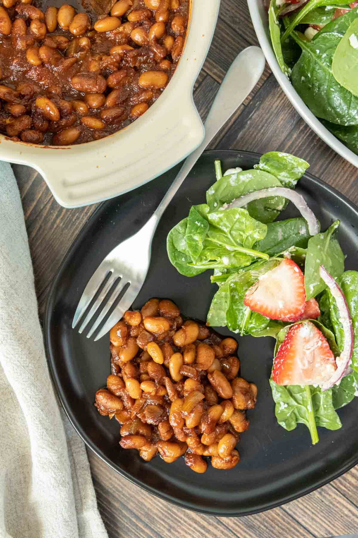 Overhead of vegetarian baked beans on a plate with salad and a fork.