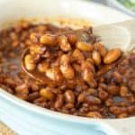 Spoonful of vegetarian baked beans being held up out of baking dish.