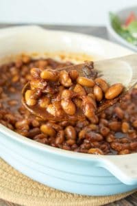 Spoonful of vegetarian baked beans being held up out of baking dish.