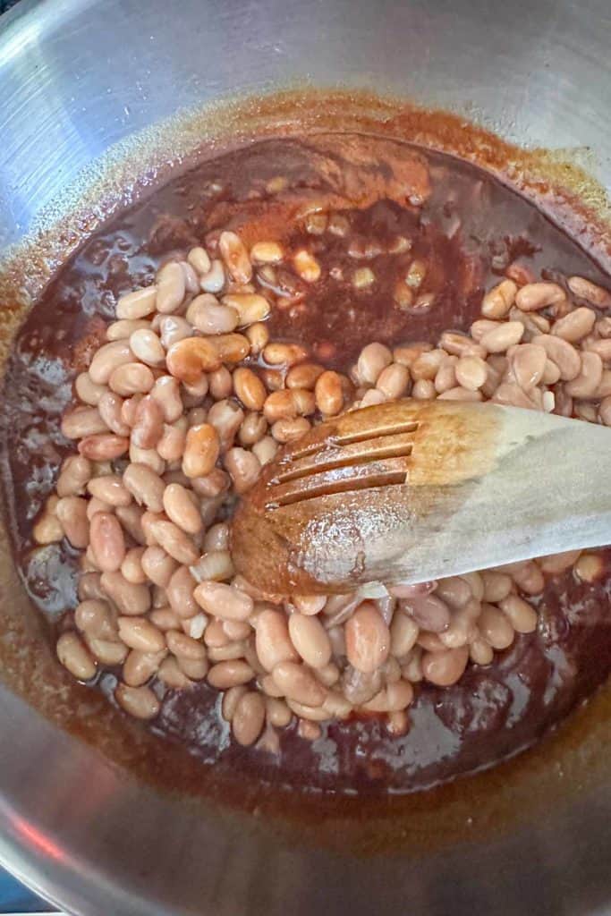 Stirring pinto beans into sauce to make vegetarian baked beans.