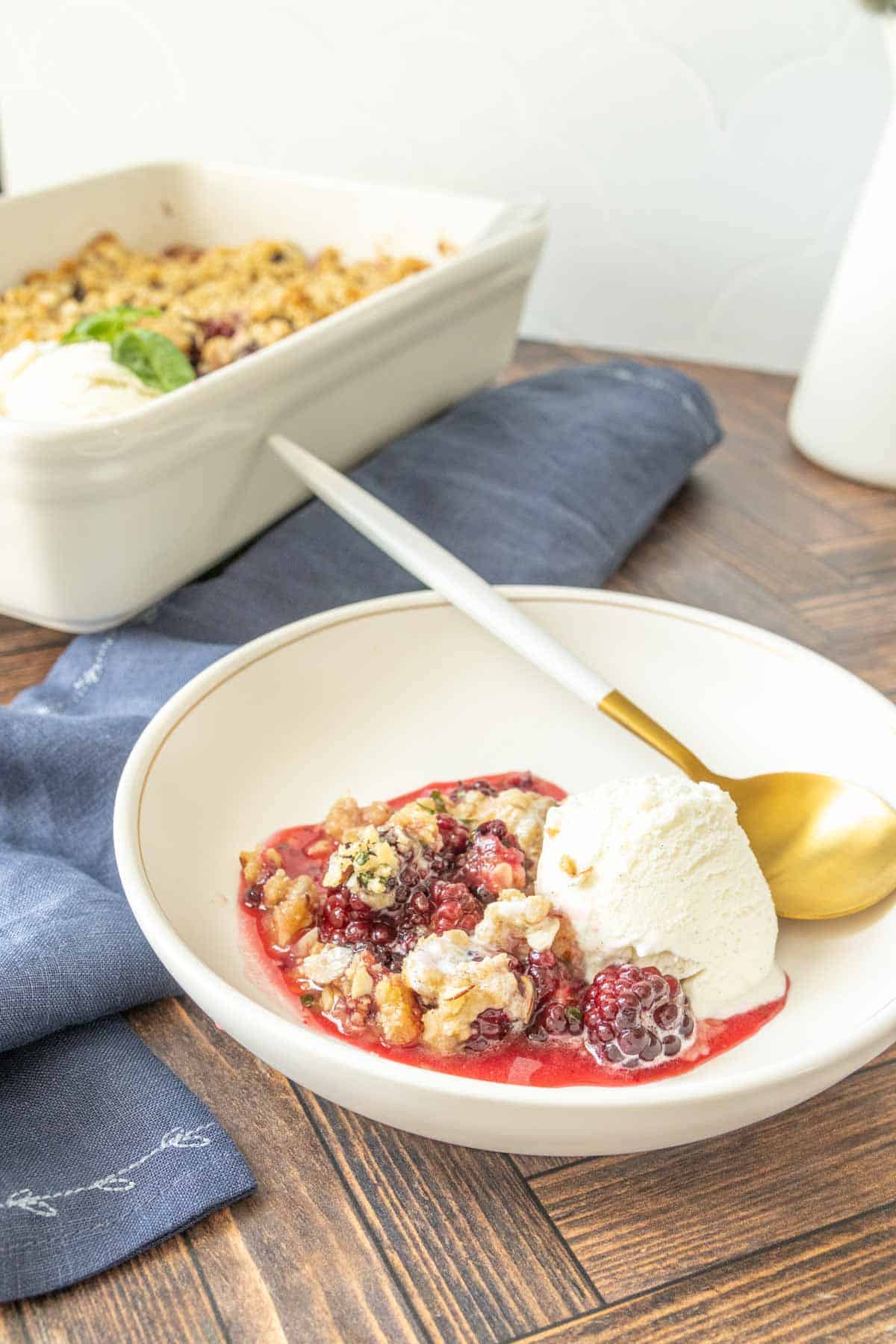 Bowl of blackberry crisp with ice cream and a gold spoon with white handle.