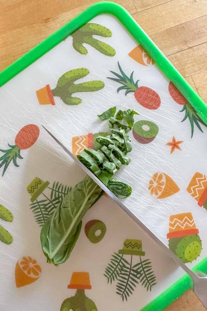 Chiffonading basil on a cutting board.