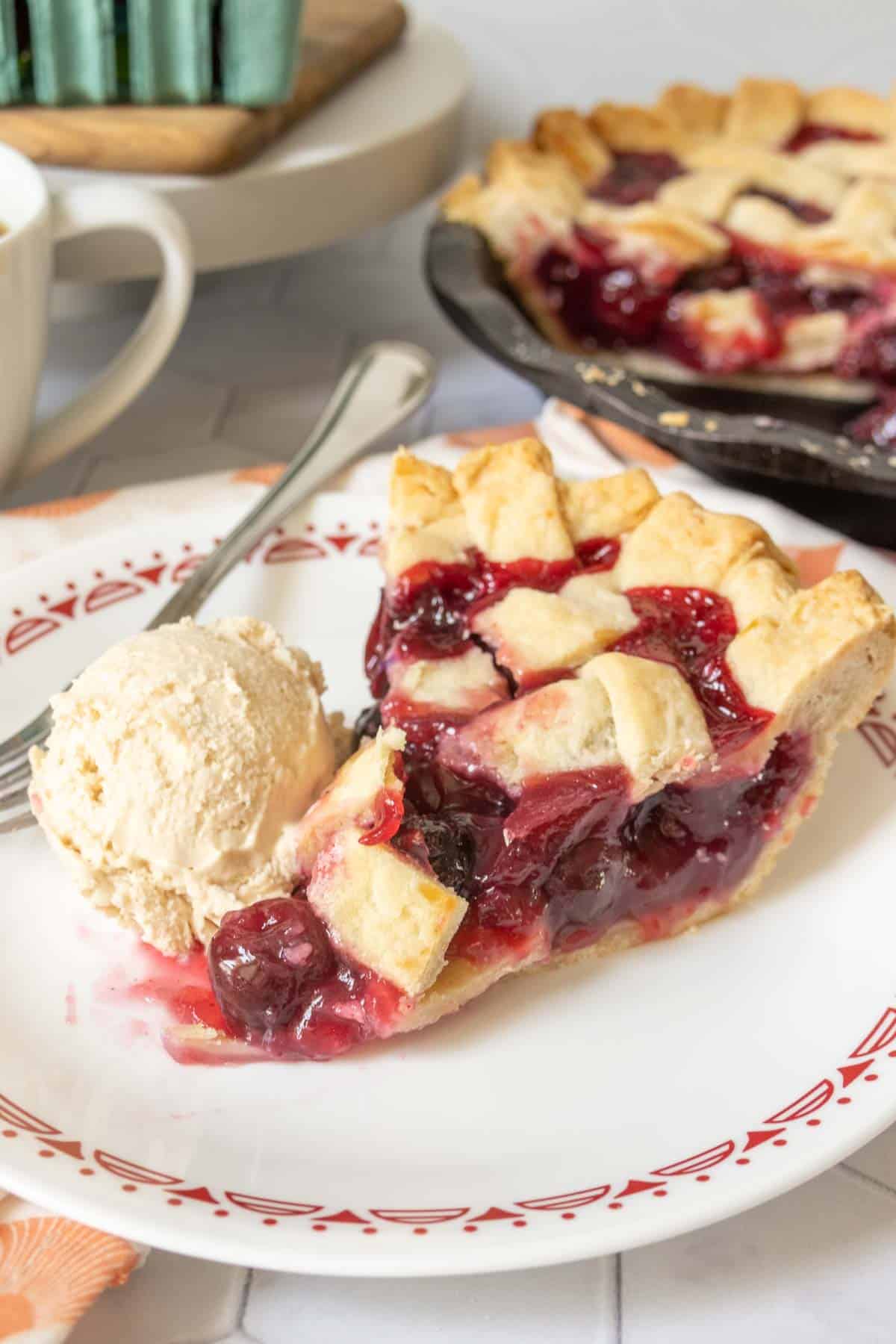 Slice of cherry pie with a scoop of ice cream beside.