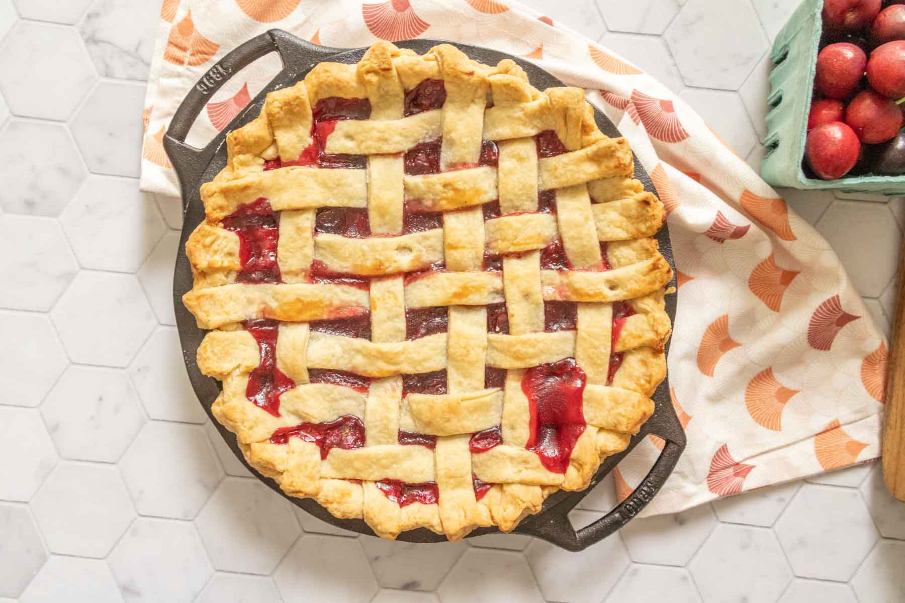 Overhead cherry pie on a tile surface with a patterned napkin.