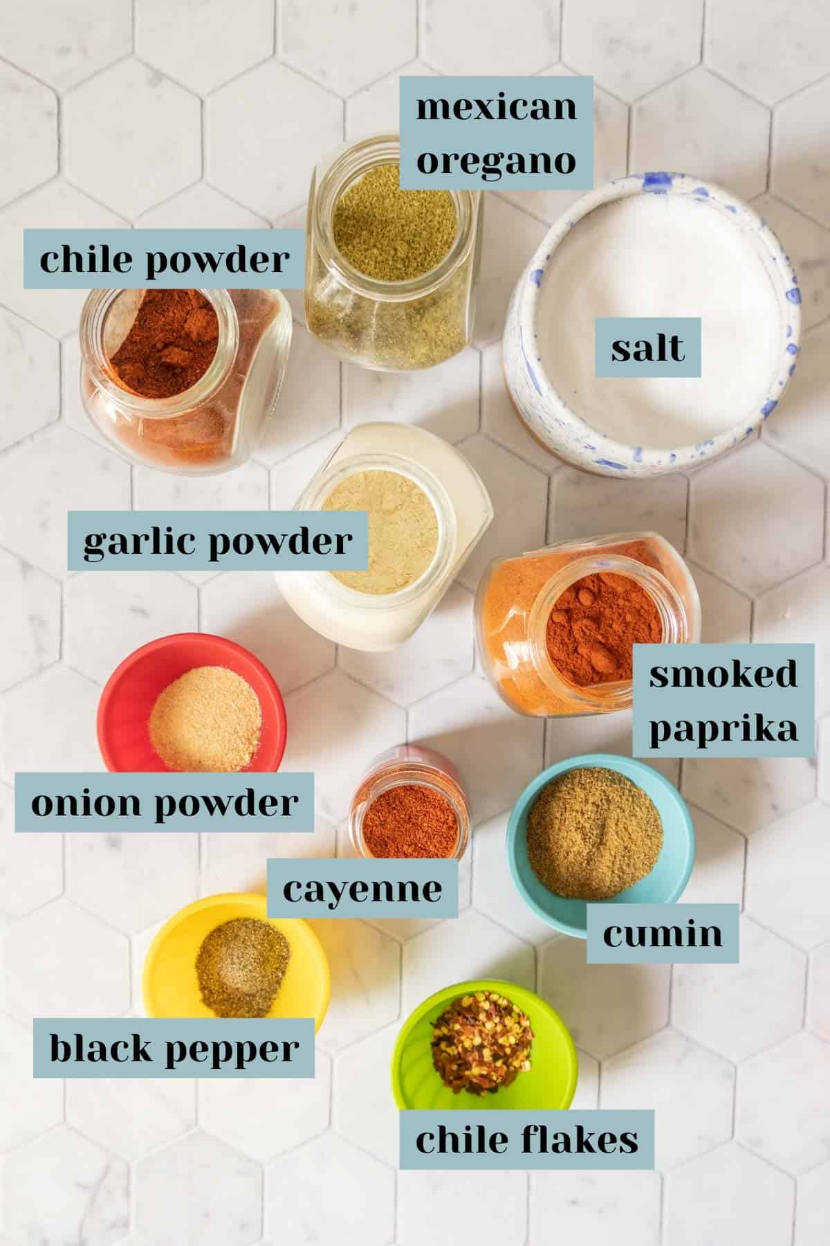 Ingredients for homemade taco seasoning on a tile surface with labels.