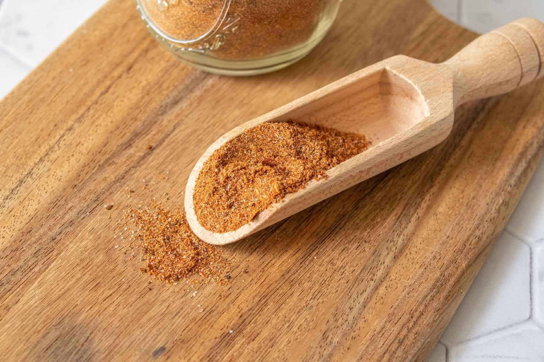 Wooden scoop of taco seasoning on a cutting board.