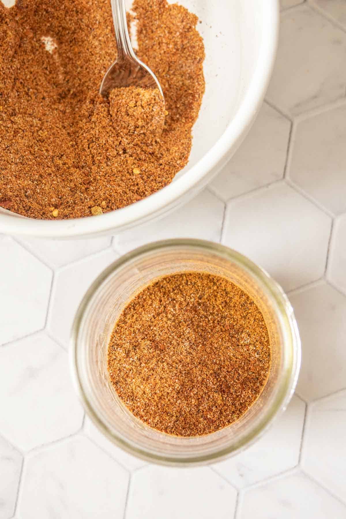 Taco seasoning in a jar next to a bowl of more seasoning.