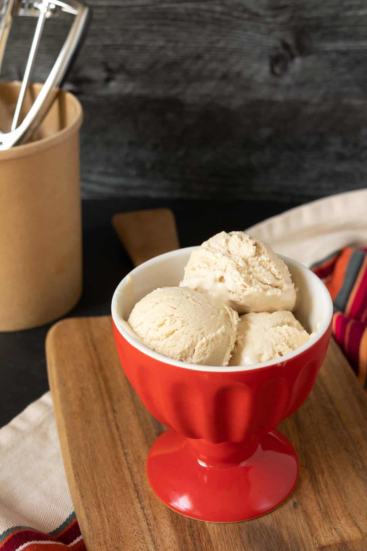 Red ice cream bowl with no-churn ice cream scoops, set on a wooden board.