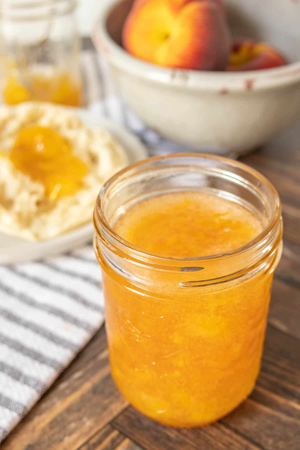 Jar of peach jam with peaches behind.