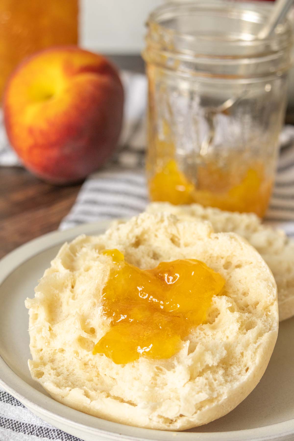 Split English muffin on a plate with a dollop of peach jam on top.