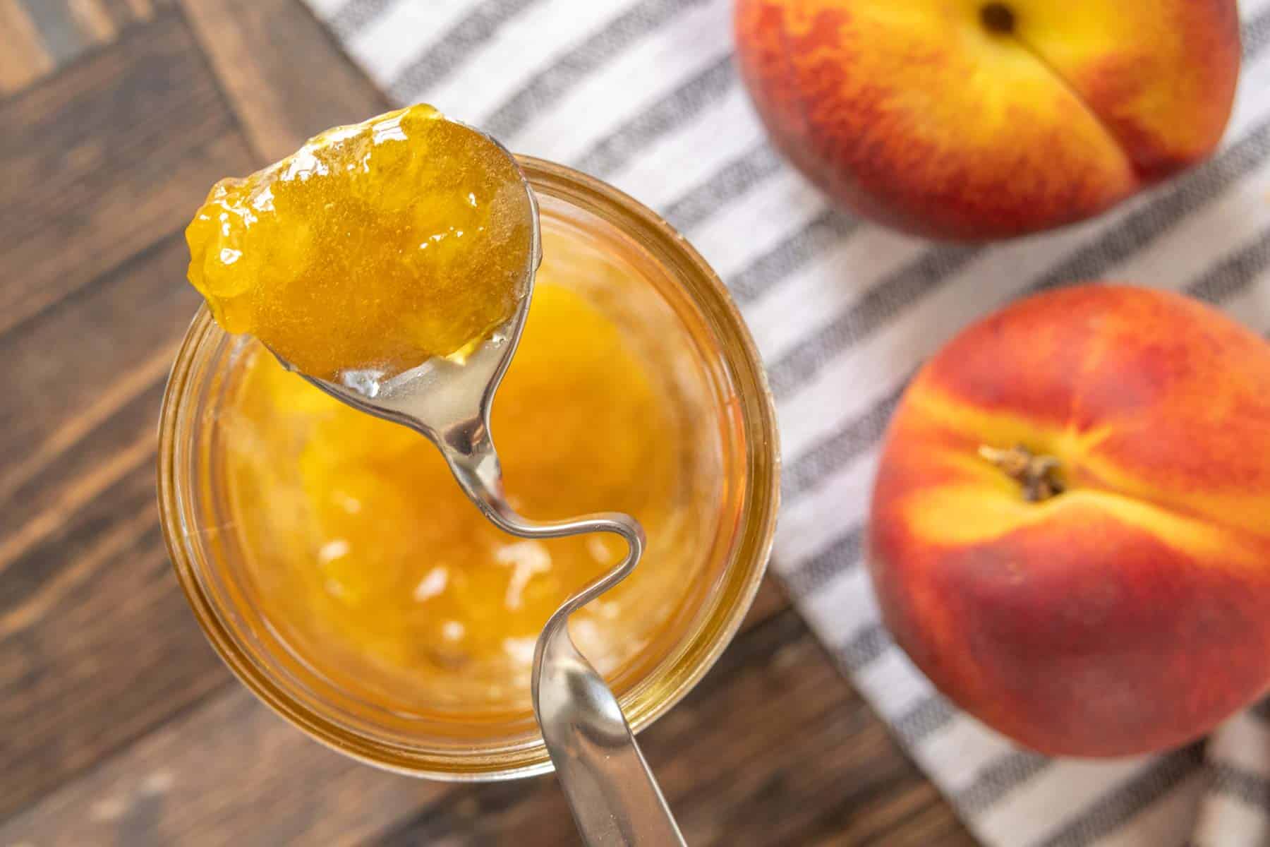 Overhead of peach jam on a spoon set on top of the jam jar.