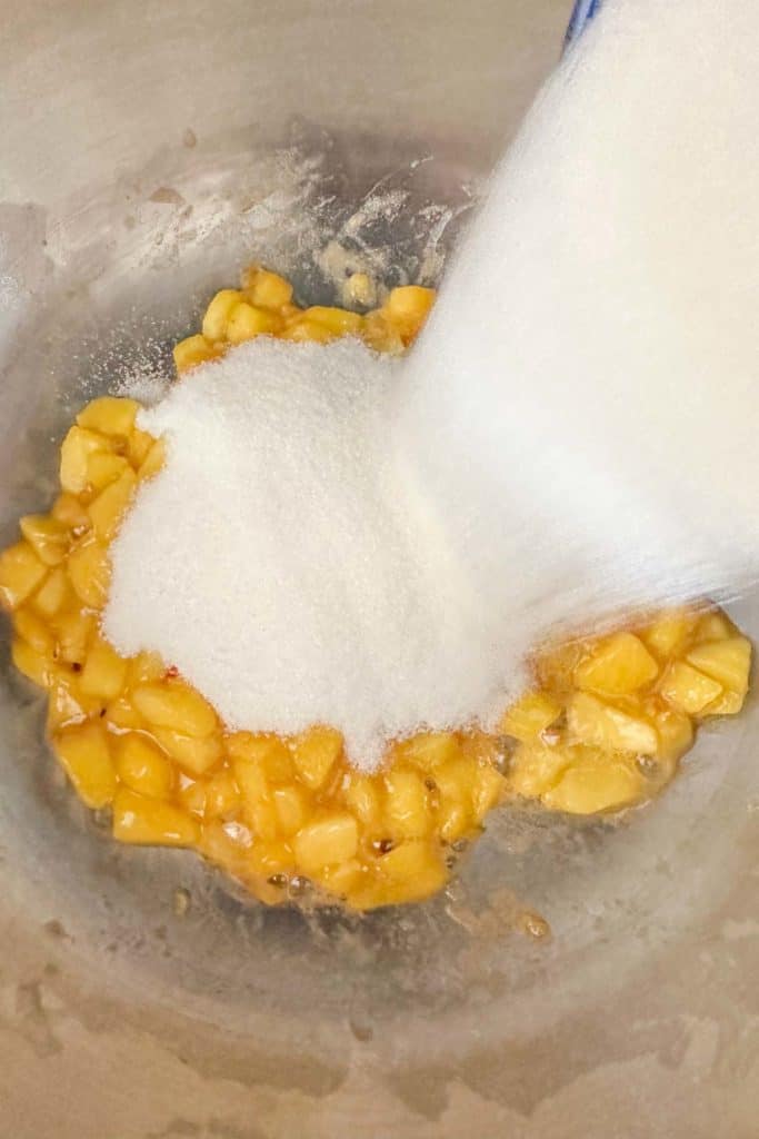 Sugar being poured into a saucepan with peaches.